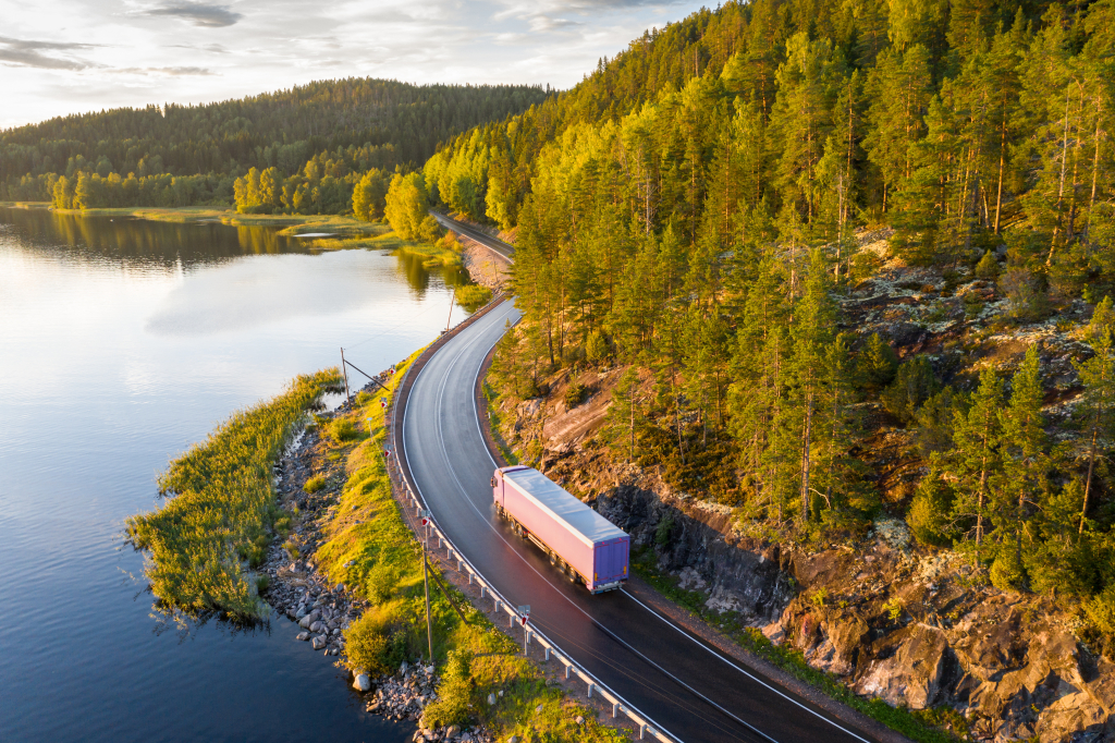 Rekka-auto ajaa metsäisen järvimaiseman halki mutkittelevaa maantietä pitkin.